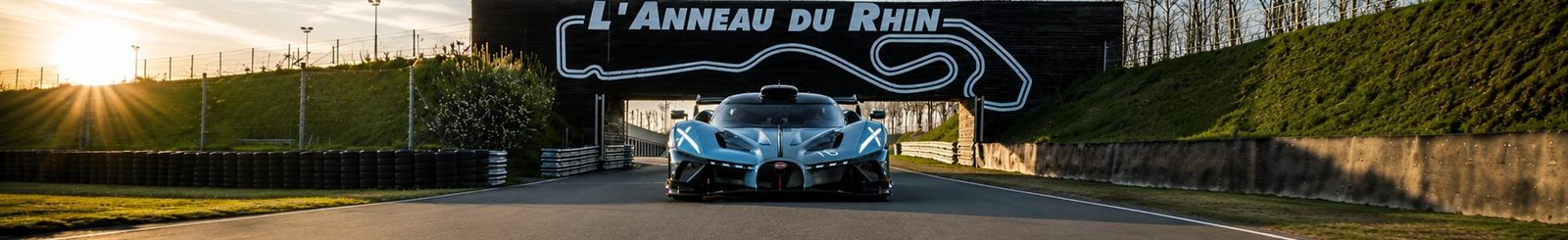Voiture de compétition sous le pont signalétique de l'Anneau du Rhin au soleil couchant