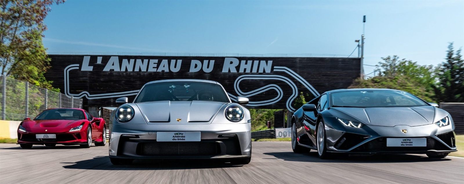 Ferrari, Porsche et Lamborghini de front devant le mur peint de l'Anneau du Rhin