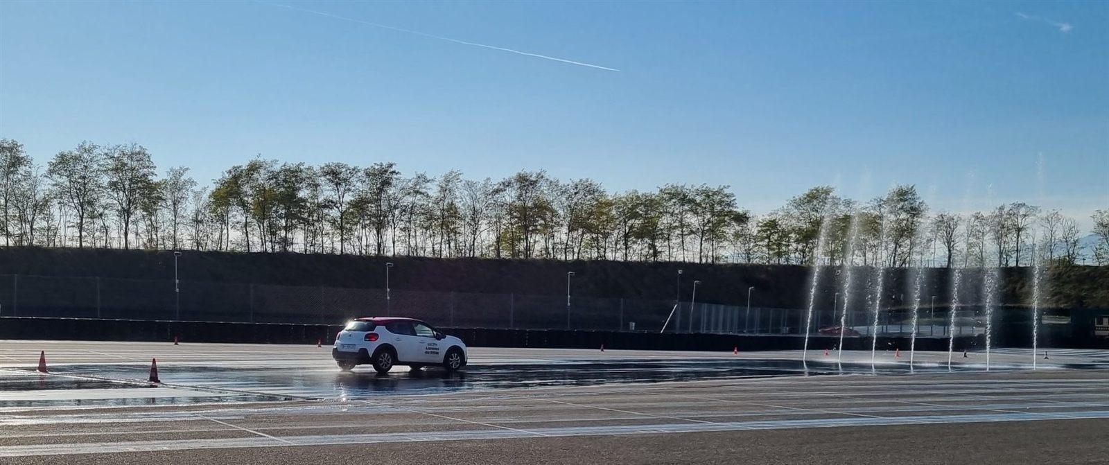 Voiture école sur le plateau arrosé, rampes d'aspersion en action